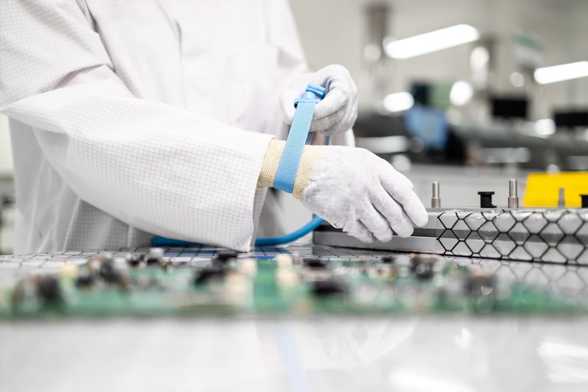 Worker putting on anti-static wristband or grounding bracelet while testing electronic components in production.