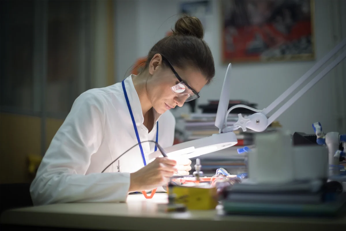 Elettricista donna di mezza età che lavora su un drone alla scrivania in un'industria, usando una lente d'ingrandimento