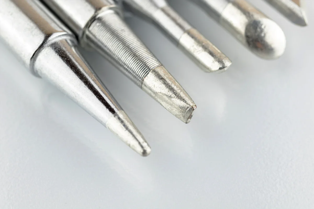 Close up of soldering tips on glass table, silver background with equipment for soldering iron